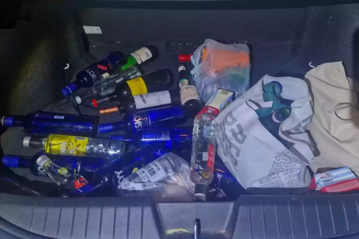 Un maletero de coche lleno de botellas vacías de alcohol y bolsas.