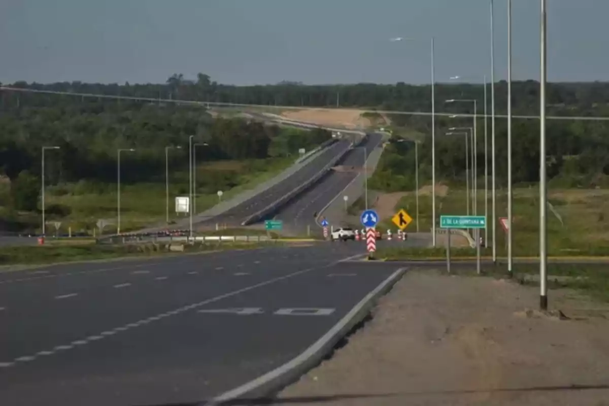 Carretera asfaltada con múltiples carriles y señales de tráfico rodeada de vegetación y postes de luz.