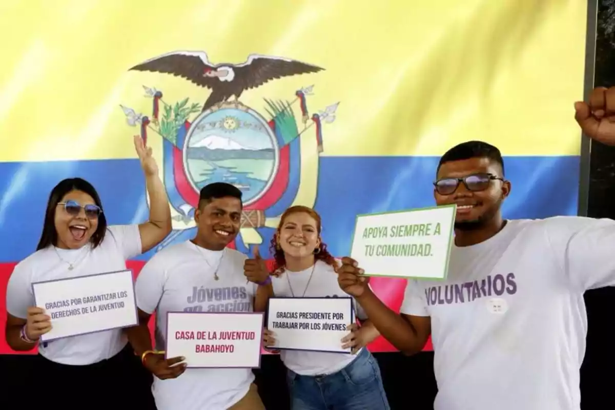 Un grupo de jóvenes sonrientes sostiene carteles con mensajes positivos frente a una bandera de Ecuador.