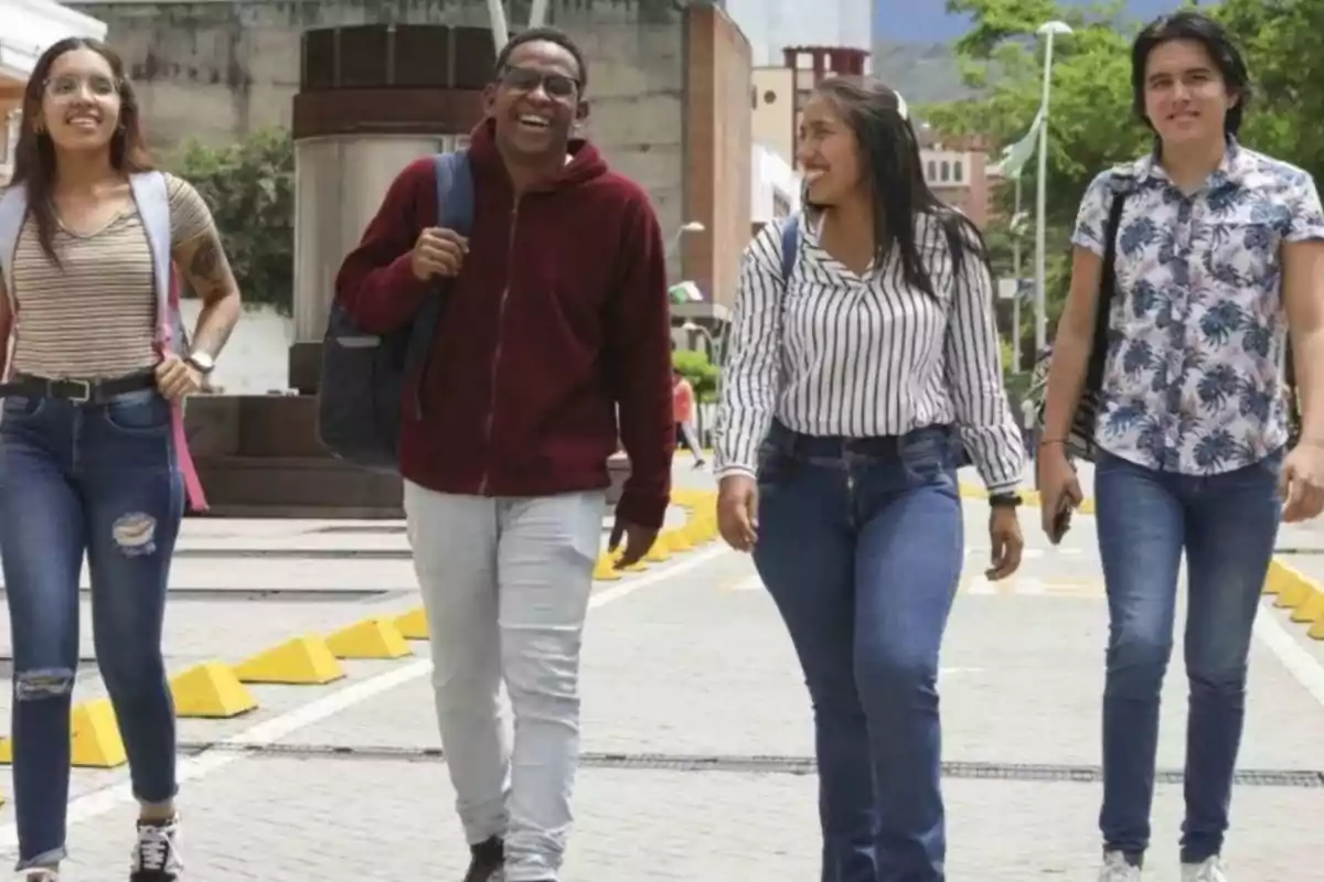 Un grupo de cuatro personas camina por una calle peatonal en un día soleado, todos llevan mochilas y parecen estar conversando y riendo.