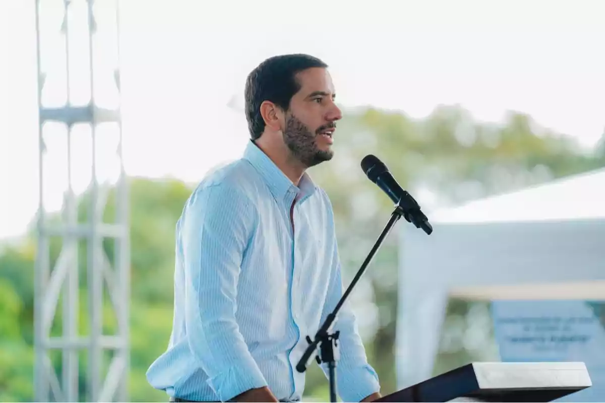 Hombre de pie hablando en un micrófono durante un evento al aire libre.