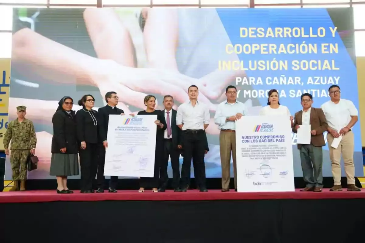 A group of people on a stage holding large signs during a development and cooperation event on social inclusion in Ecuador.