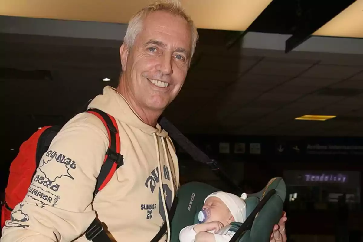 Un hombre sonriente lleva a un bebé dormido en un portabebés en un lugar público.