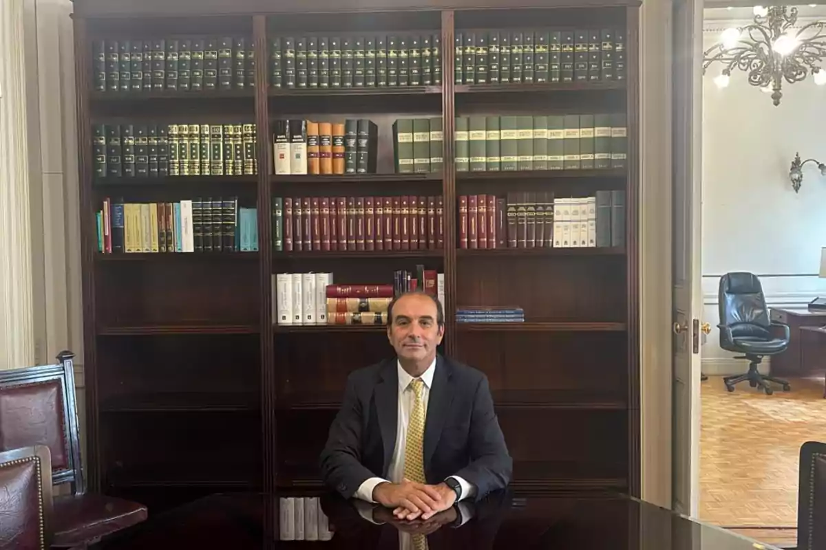 A man sitting at a desk in an office with bookshelves full of books behind him.