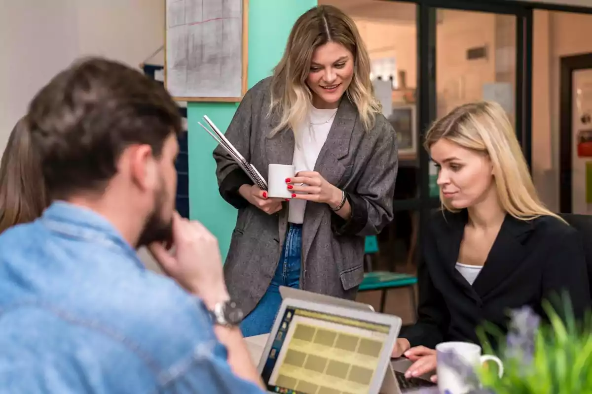 A group of people in an office collaborating and conversing while looking at a laptop.