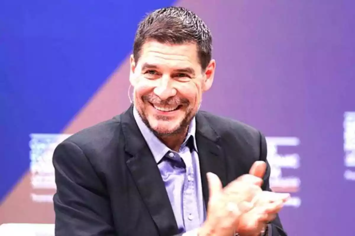 Un hombre sonriente aplaudiendo en un evento con fondo azul. Un hombre sonriente aplaudiendo en un evento con fondo azul.