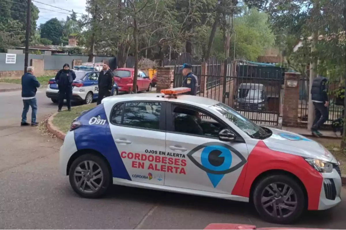A police car with the logo "Cordobeses en Alerta" is parked on a street, while several officers and people are gathered around.