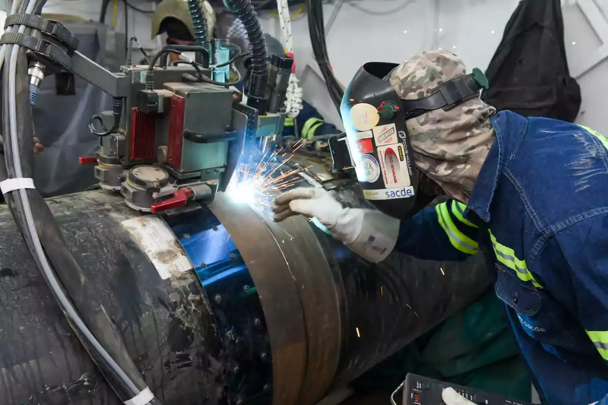 Worker with protective equipment welding an industrial pipe using an automatic machine while sparks fly Worker with protective equipment welding an industrial pipe using an automatic machine while sparks fly