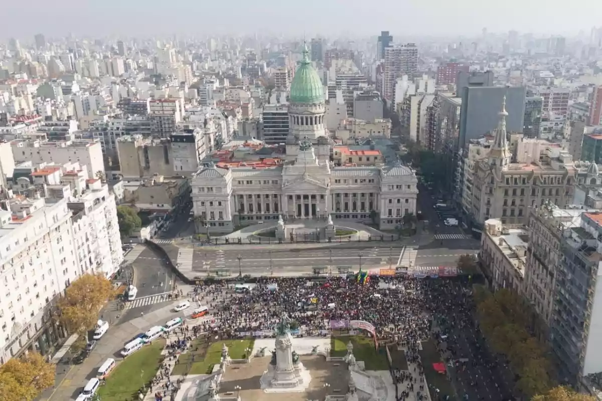 Aerial view of the Argentine National Congress with a crowd gathered in the square in front of the building, surrounded by city streets and buildings in Buenos Aires.