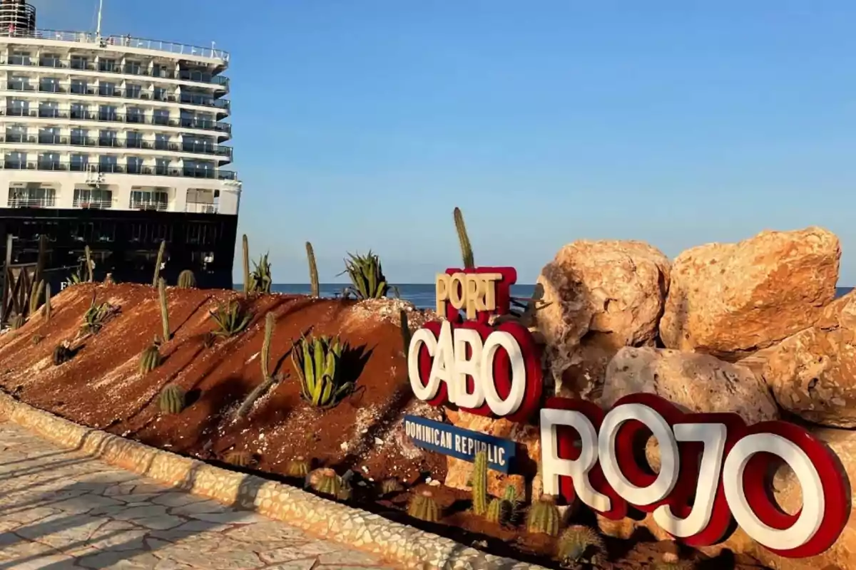 Un crucero atracado junto a un letrero colorido de Port Cabo Rojo en República Dominicana rodeado de cactus y grandes rocas bajo un cielo despejado