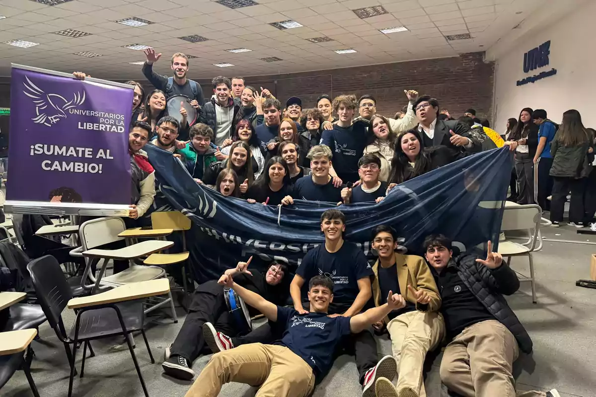 Group of young people in a university classroom posing together and holding banners of Students for Liberty and a sign inviting others to join the change