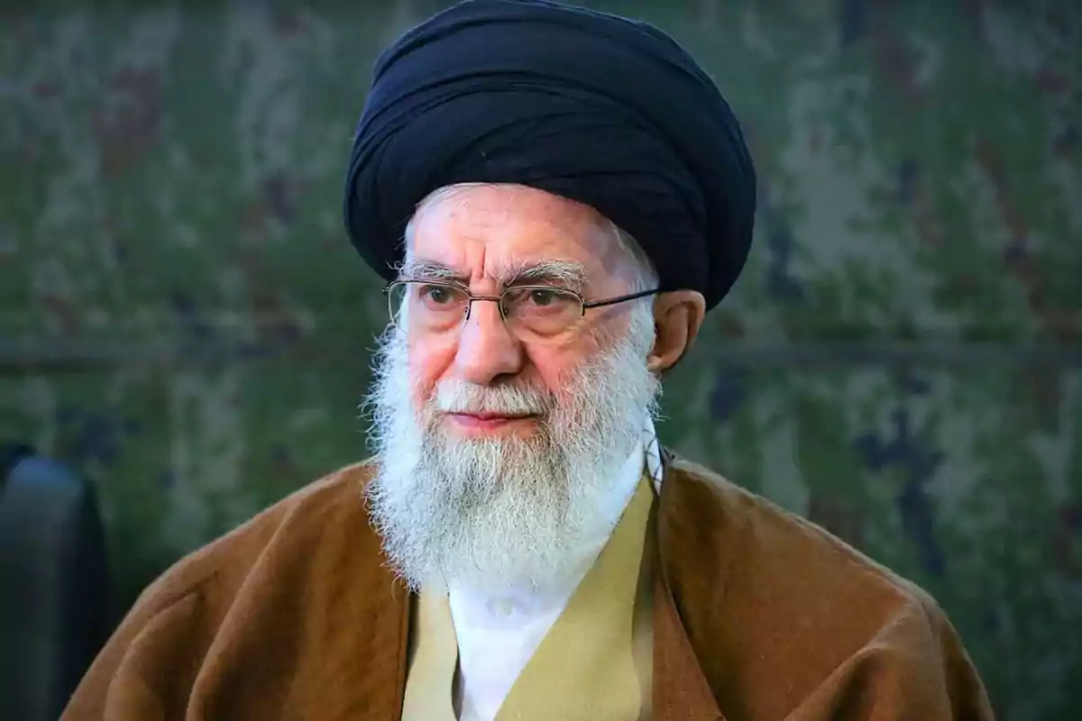 Older man with a white beard, wearing glasses and a black turban, dressed in traditional clothing and standing in front of a blurred background. Older man with a white beard, wearing glasses and a black turban, dressed in traditional clothing and standing in front of a blurred background.