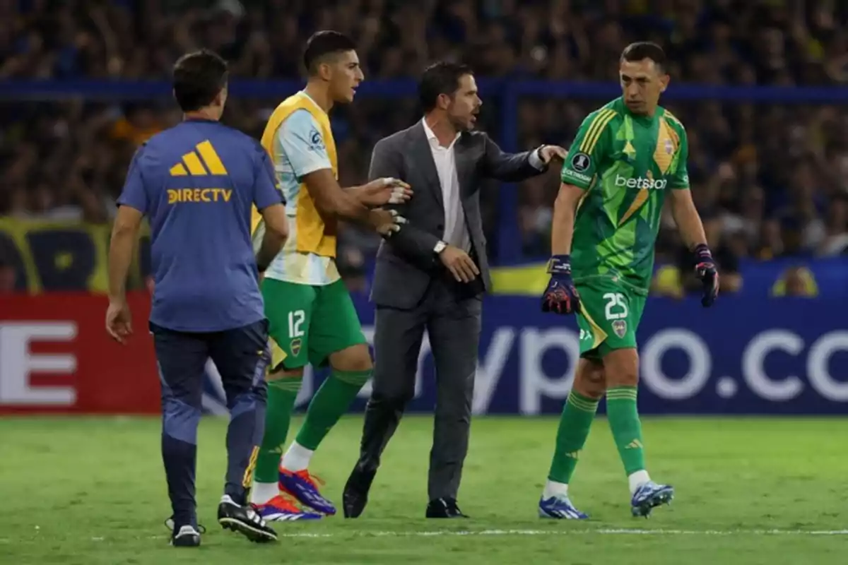 Un grupo de personas en un campo de fútbol, una de ellas con uniforme verde y guantes, mientras otra persona con traje parece estar dando instrucciones. Un grupo de personas en un campo de fútbol, una de ellas con uniforme verde y guantes, mientras otra persona con traje parece estar dando instrucciones.