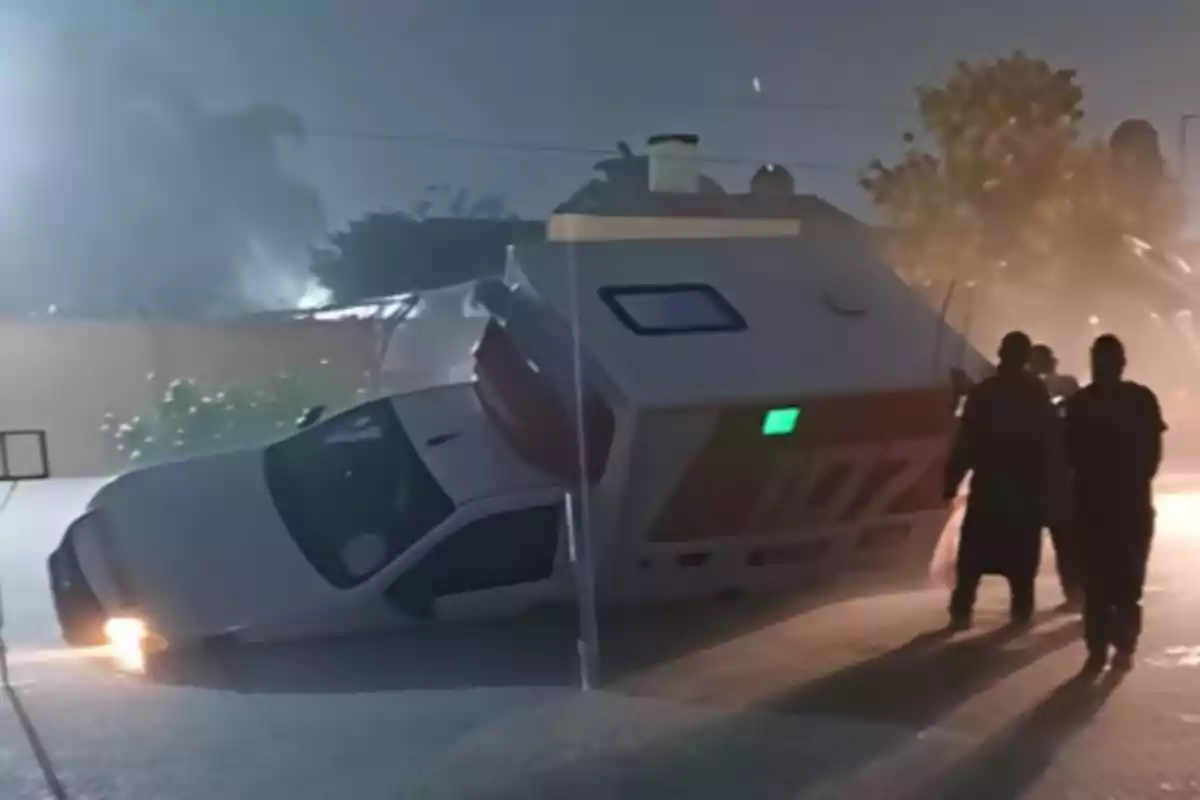 An ambulance tipped over on its side on a street at night with several people watching the scene. An ambulance tipped over on its side on a street at night with several people watching the scene.