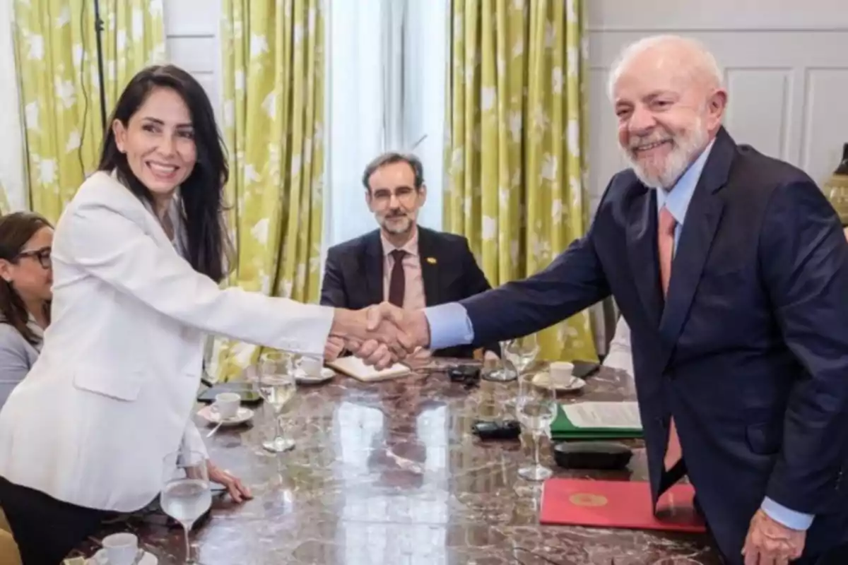 People shaking hands at a formal meeting around a marble table with yellow curtains in the background.