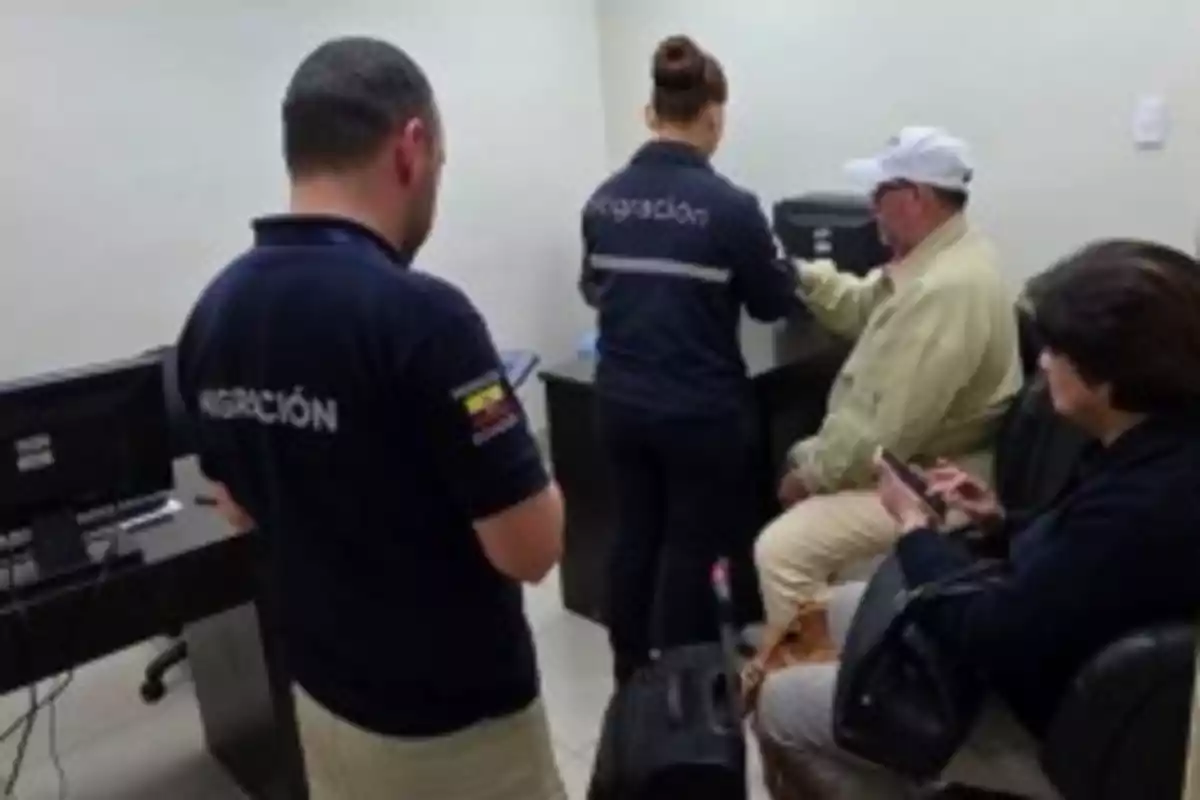 Personas en una oficina de migración, una de ellas está siendo atendida por un oficial mientras otra espera sentada. Personas en una oficina de migración, una de ellas está siendo atendida por un oficial mientras otra espera sentada.