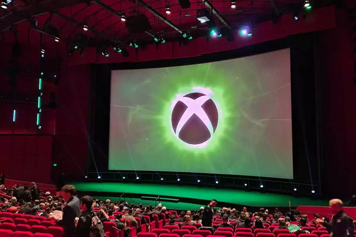 Auditorium full of people with a large screen displaying the Xbox logo on stage Auditorium full of people with a large screen displaying the Xbox logo on stage
