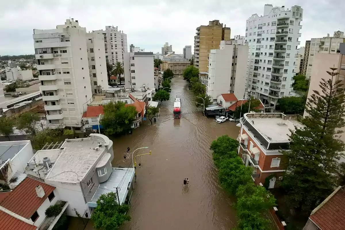 A flooded street in a city with tall buildings and vehicles partially submerged in water.