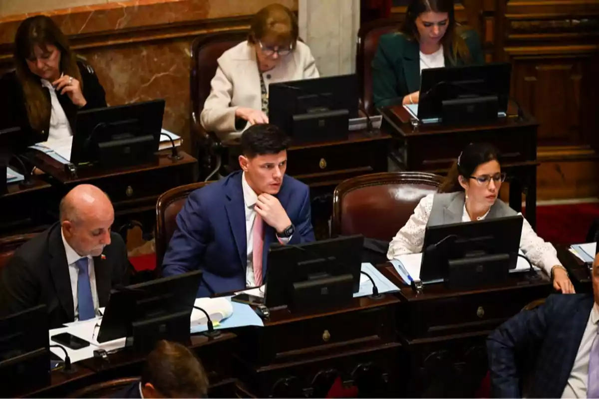 Personas trabajando en un entorno de oficina con computadoras portátiles y documentos sobre escritorios de madera. Personas trabajando en un entorno de oficina con computadoras portátiles y documentos sobre escritorios de madera.