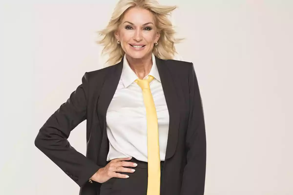 Mujer rubia sonriente vestida con traje negro, camisa blanca y corbata amarilla