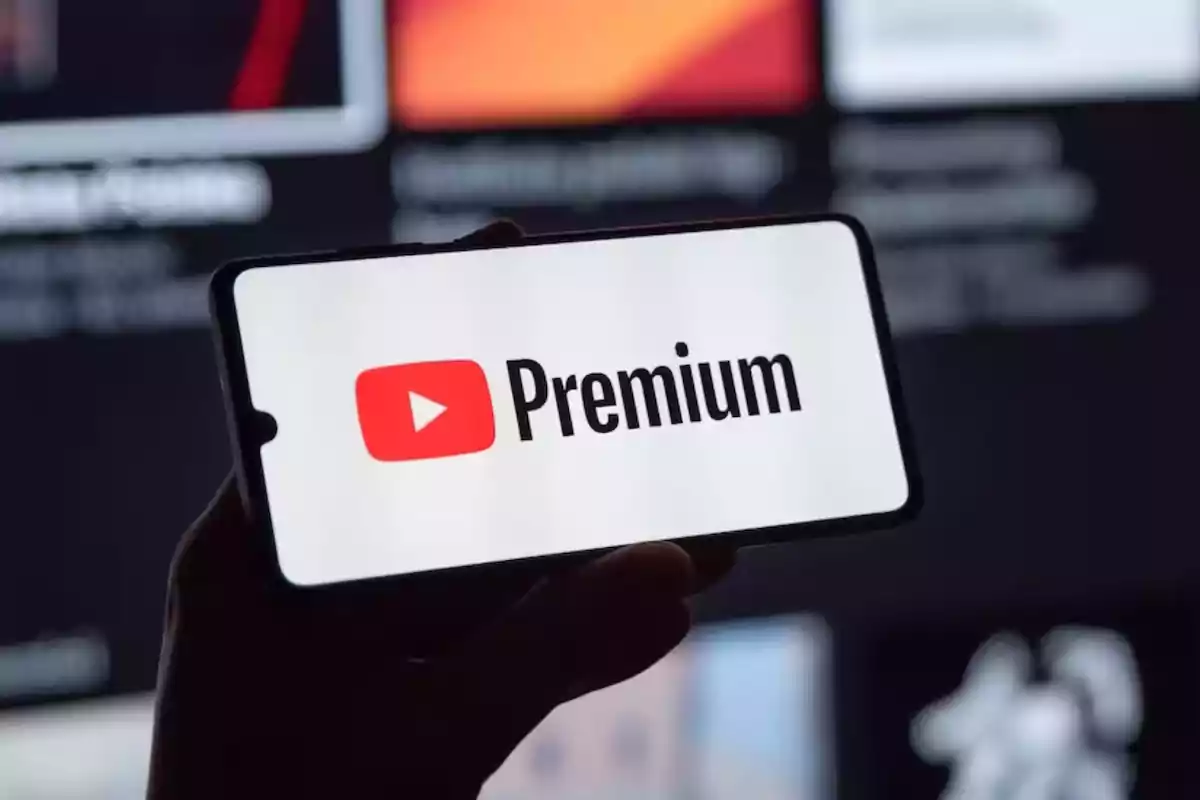A hand holds a mobile phone displaying the YouTube Premium logo on the screen. A hand holds a mobile phone displaying the YouTube Premium logo on the screen.