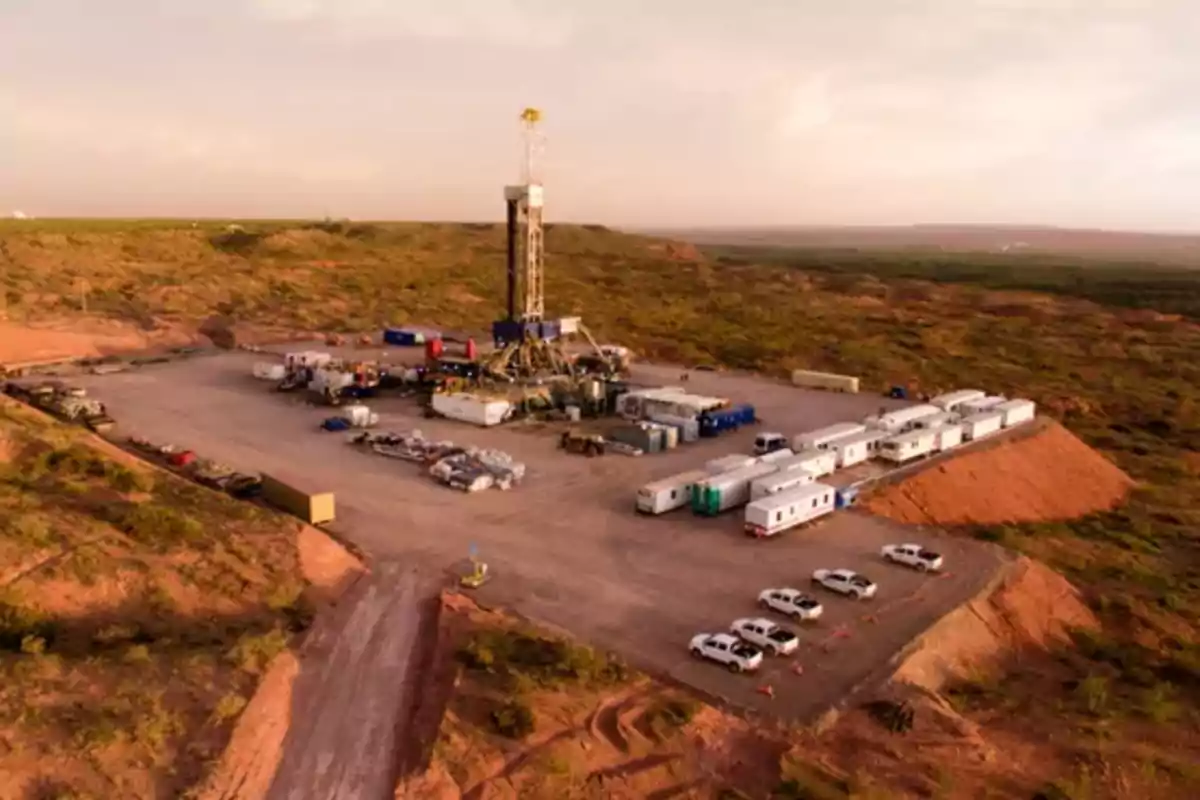 Vista aérea de un sitio de perforación petrolera rodeado de vegetación y vehículos estacionados.