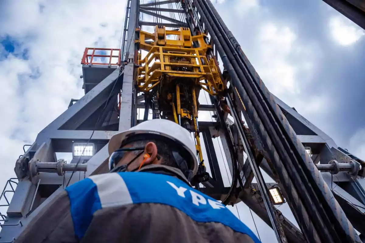 Trabajador con casco y equipo de seguridad en una plataforma petrolera bajo un cielo nublado.