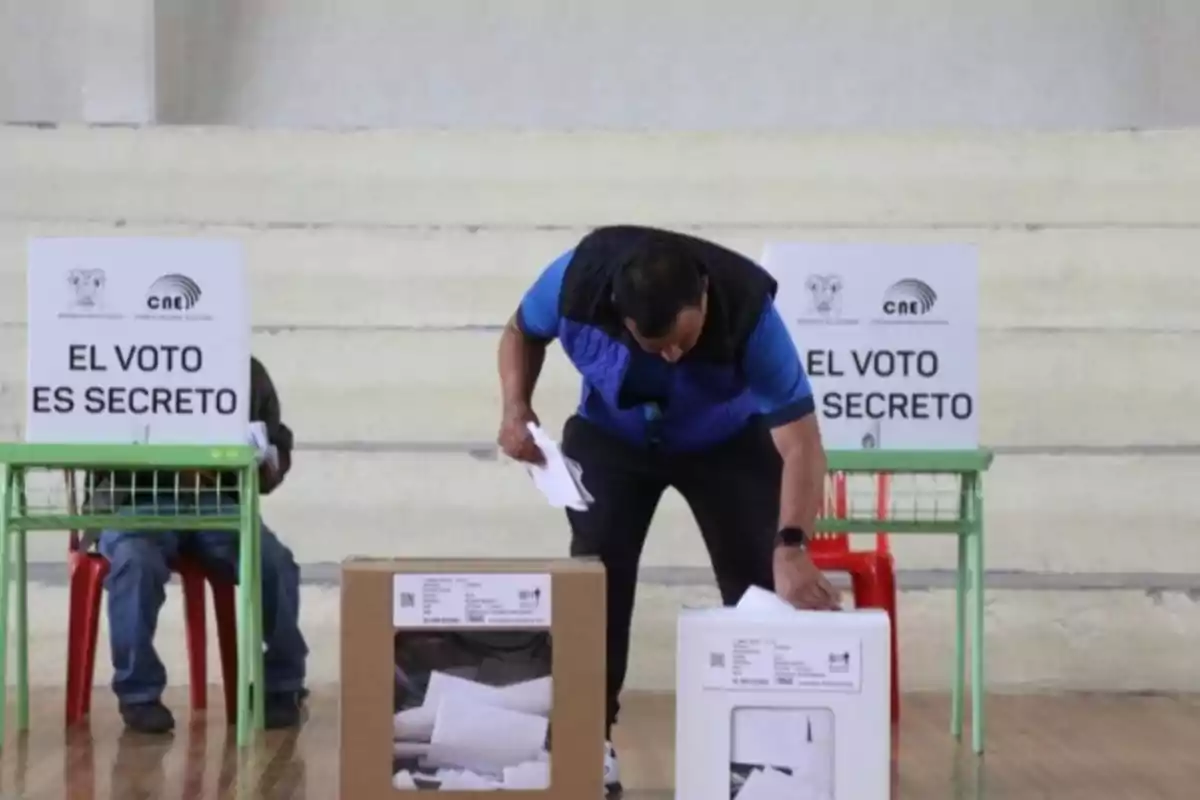 Una persona depositando su voto en una urna en un centro de votación con carteles que indican "El voto es secreto".