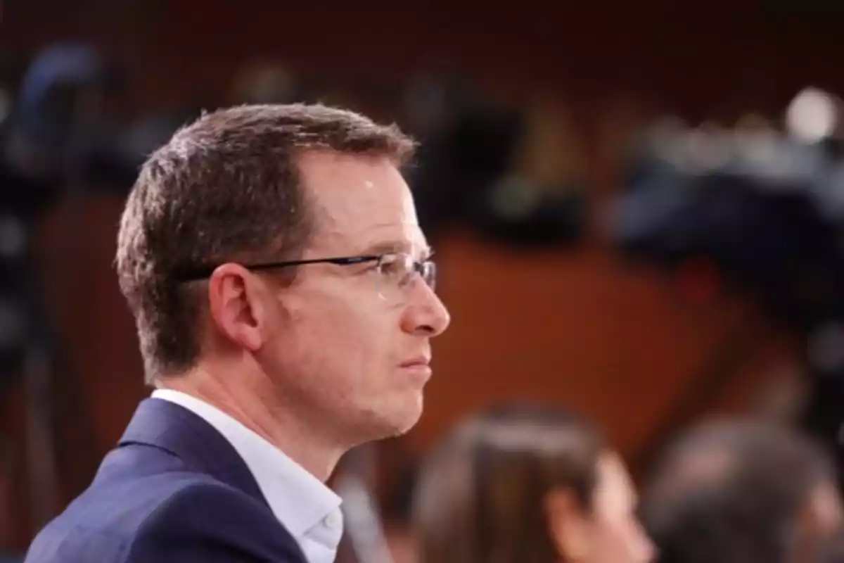 Man in profile wearing glasses and a blue jacket in an indoor setting with a blurred background Man in profile wearing glasses and a blue jacket in an indoor setting with a blurred background