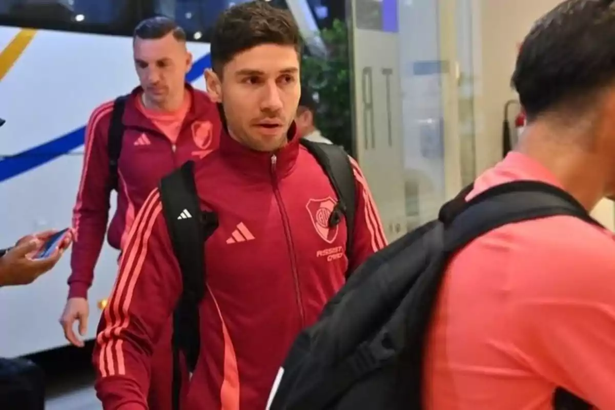 A group of people in red sportswear and backpacks walks in an indoor area near a bus. A group of people in red sportswear and backpacks walks in an indoor area near a bus.